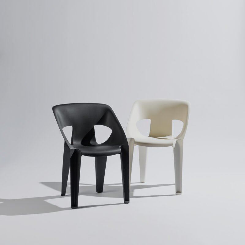 Schwarze und weiße Arco-Stühle sind in einem stilvollen Fotostudio vor neutralem Hintergrund und sanfter Beleuchtung arrangiert, wobei das elegante Design und der Kontrast zwischen den Farben im Mittelpunkt stehen.