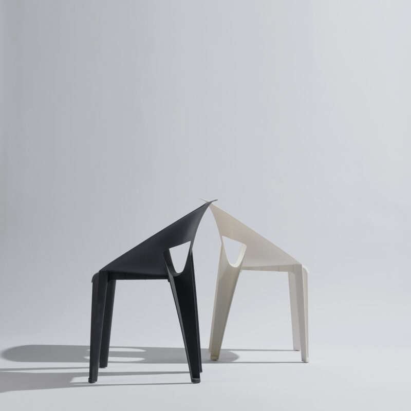 Schwarze und weiße Arco-Stühle sind in einem stilvollen Fotostudio vor neutralem Hintergrund und sanfter Beleuchtung arrangiert, wobei das elegante Design und der Kontrast zwischen den Farben im Mittelpunkt stehen.