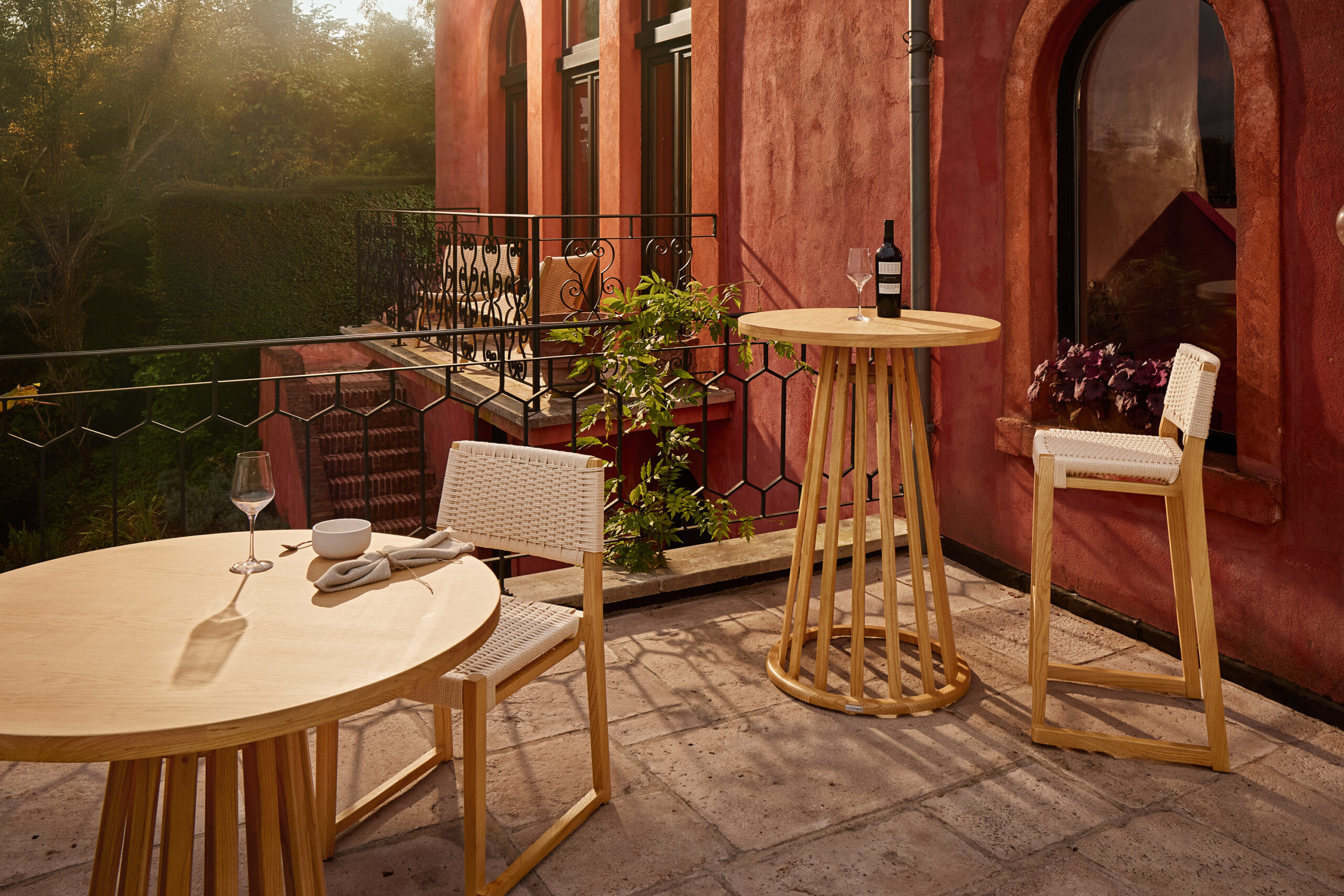 Flexfurn Mundi collectie: lage ronde tafel en hoge bartafel met houten stoelen op een zonnig terras