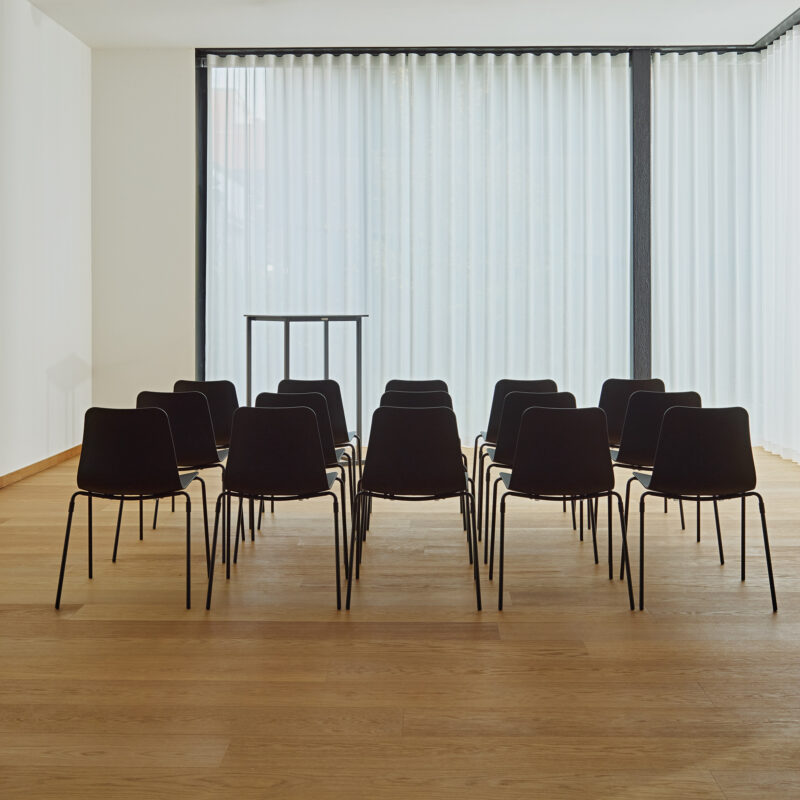 Salle de réunion sobre avec des chaises Cruvo disposées en trois rangées nettes pour une présentation, privilégiant un cadre élégant et fonctionnel.